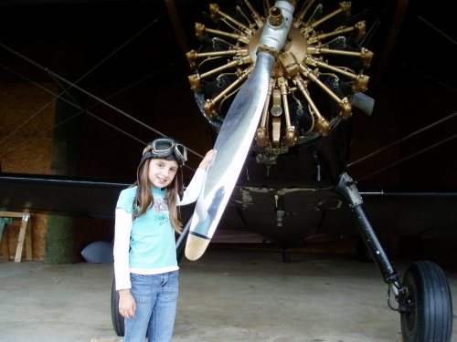 Emily with her goggles up beside a radial-engine biplane